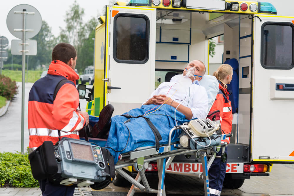 Eine Rettungssanitäterin und ein Notfallsanitäter transportieren einen Patienten auf einer Liege zum Krankenwagen.