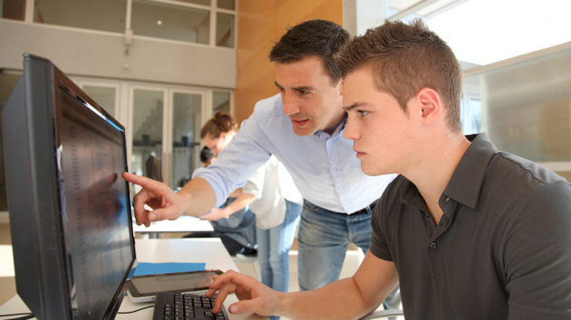 Ein Ausbilder hilft einem Auszubildenden bei der Arbeit am Computer.