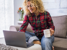 Eine Frau sitzt lächelnd mit einer Tasse vor dem Computer
