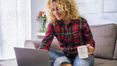 Eine Frau sitzt lächelnd mit einer Tasse vor dem Computer