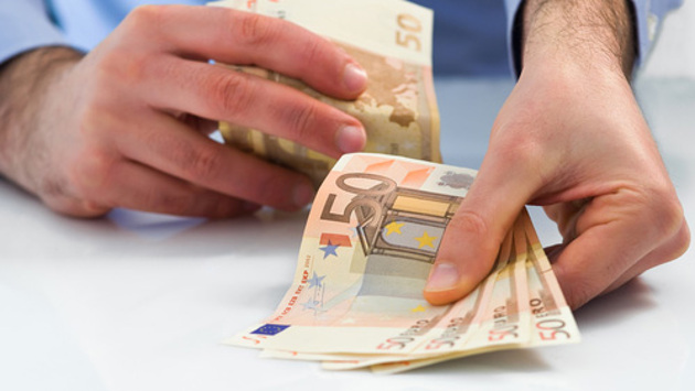 Ein Mann reicht vier 50-Euro-Scheine in Richtung Betrachter und behält weitere Geldscheine in der anderen Hand.