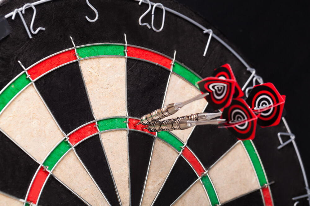 3 Drei Darts-Pfeile stecken in der Triple 20 eines Darts-Boards