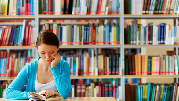 Eine Studentin sitzt in der Bibliothek und liest ein Buch.