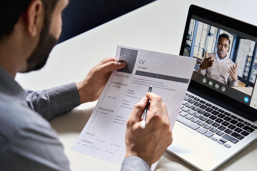 Personalverantwortlicher, Personalvermittler oder Arbeitgeber mit Lebenslauf in der Hand, der online ein virtuelles Vorstellungsgespräch mit einem afrikanischen Bewerber per Videoanruf führt. 