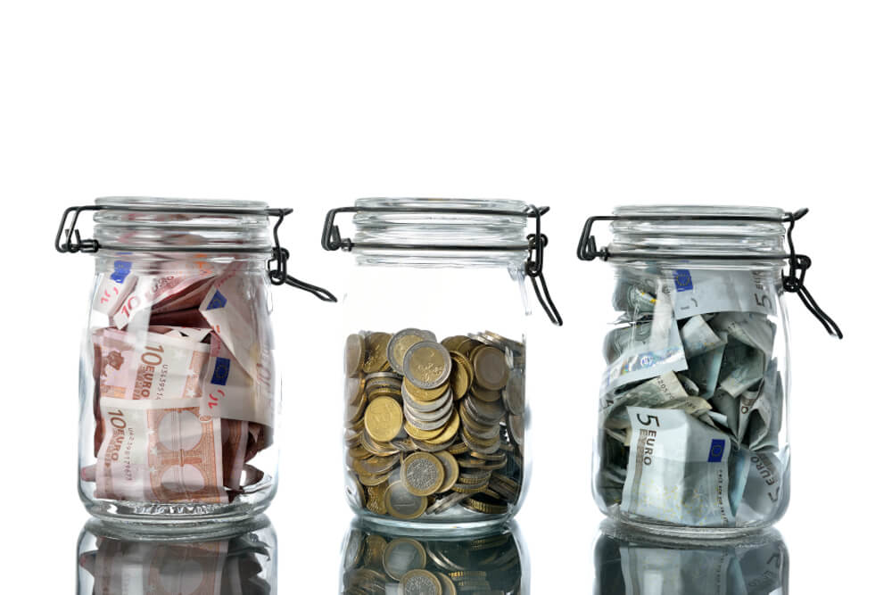 Drei transparente Einmachgläser mit unterschiedlich vielen Euros befüllt.