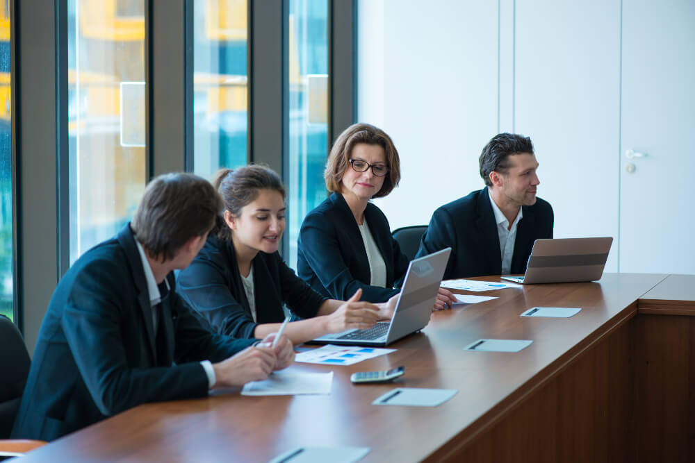Mehrere Wirtschaftsprüferinnen und Wirtschaftsprüfer besprechen sich in einem Meeting-Raum.
