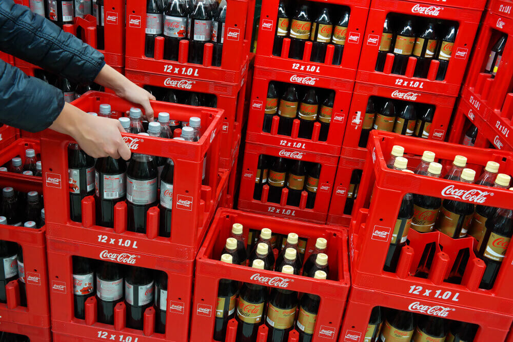 Ein Mitarbeiter stapelt Coca-Cola-Kisten in einem Getränke-Lager.