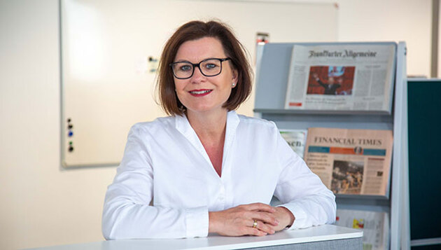 Marion Weckes, ehemalige Vergütungsexpertin der Hans-Böckler-Stiftung sitzt vor Zeitungen und lächelt.