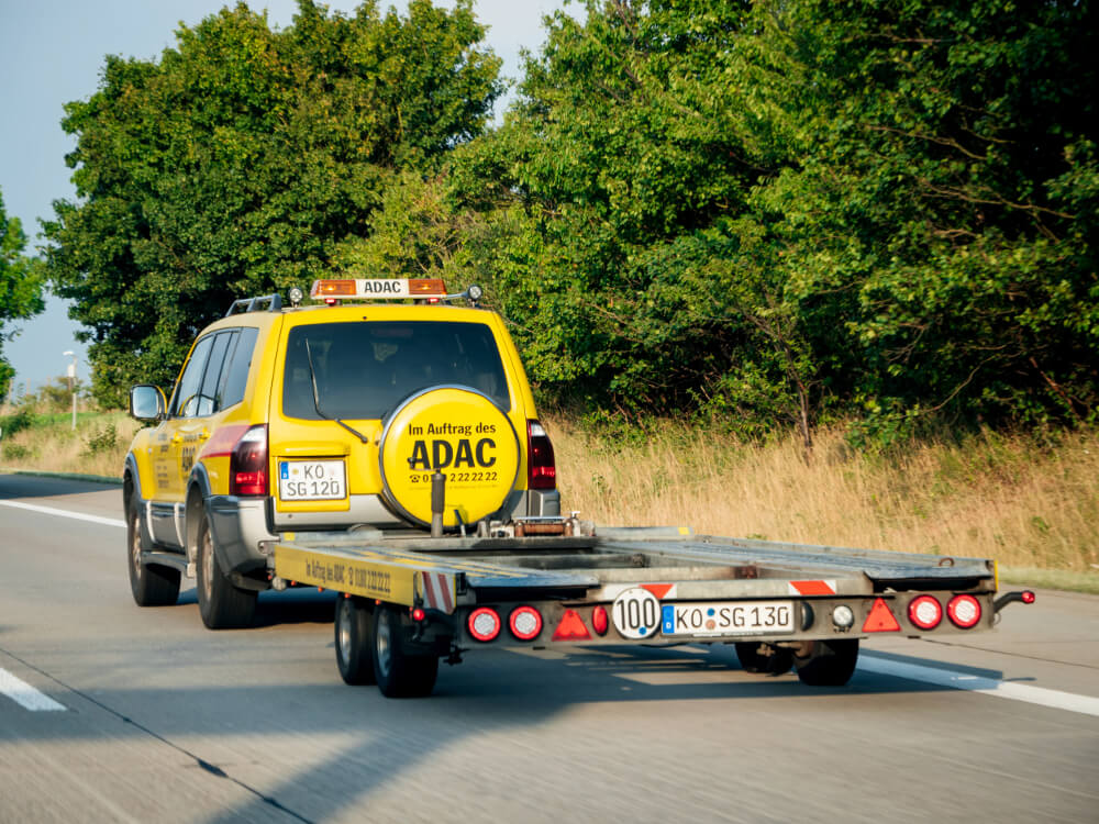 Ein Geländewagen des ADAC fährt mit einem leeren Anhänger auf einer Landstraße.