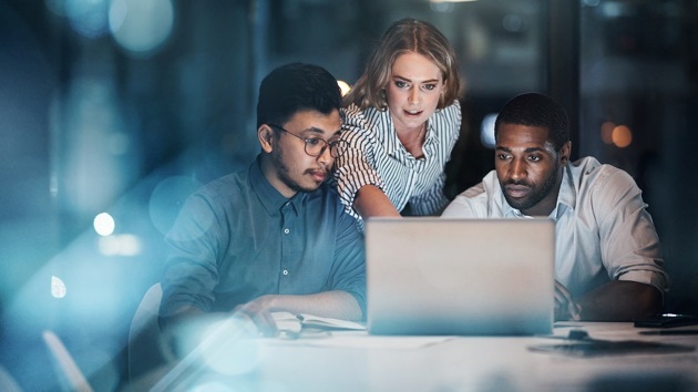 Drei Personen arbeiten spät am Laptop