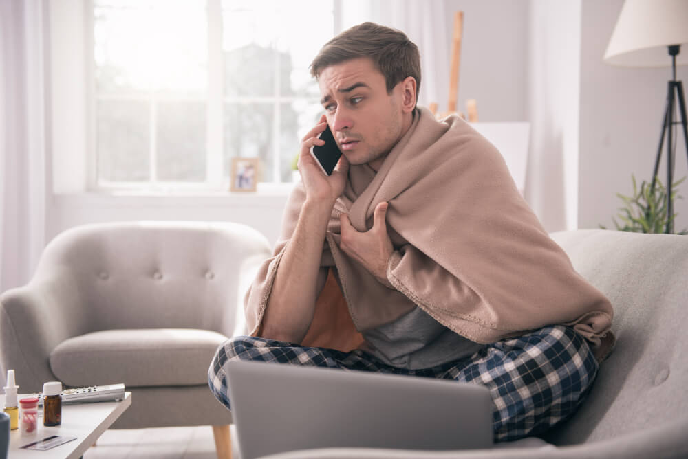 Ein krank aussehender Mann sitzt auf dem Sofa und telefoniert.