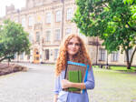 Eine junge Studentin steht vor einem Universitätsgebäude im Ausland.