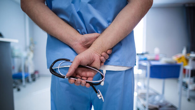 Ein Internist verschränkt die Arme hinter dem Rücken und hält ein Stethoskop.