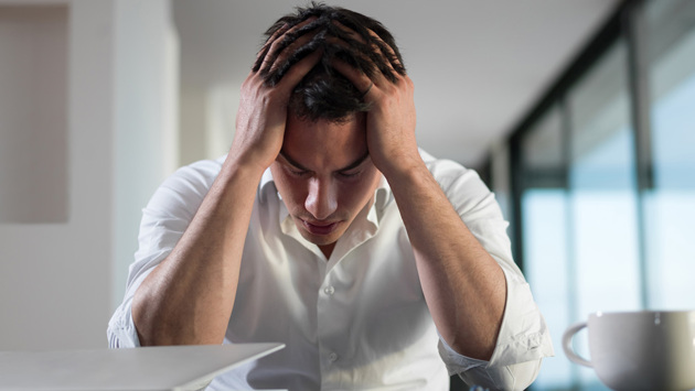 Ein Mann in Bluse sitzt am Tisch und stützt seinen Kopf verzweifelt mit seinen Händen.