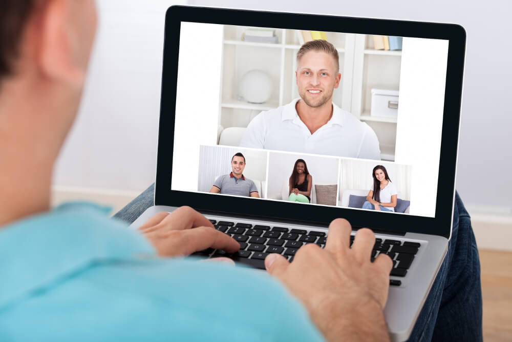 Ein junger Mann nimmt vom Homeoffice aus an einer Videokonferenz mit Kolleginnen und Kollegen teil.