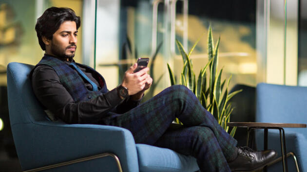 Junger Mann, der auf dem Sofa sitzend ein Mobiltelefon benutzt