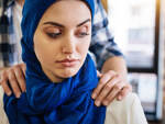 Sexuelle Belästigung am Arbeitsplatz: Muslimische Frau sitzt, während ein Mann sie belästigt.