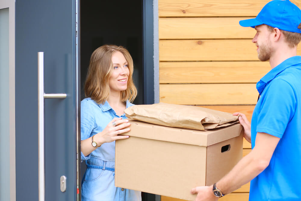 Ein Hermes-Paketbote übergibt einer Empfängerin ein Paket an der Haustür.