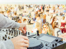 Hände eines DJs, der Musik gegen eine Menschenmenge am Strand mischt