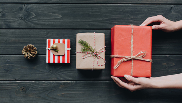 Hände umfassen eine Geschenkbox, davor sind zwei kleinere Boxen und ein Tannenzapfen.